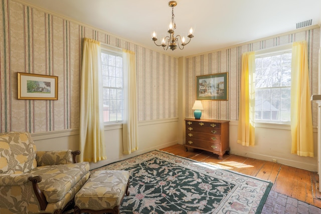 living area featuring light wood finished floors, wallpapered walls, visible vents, and an inviting chandelier