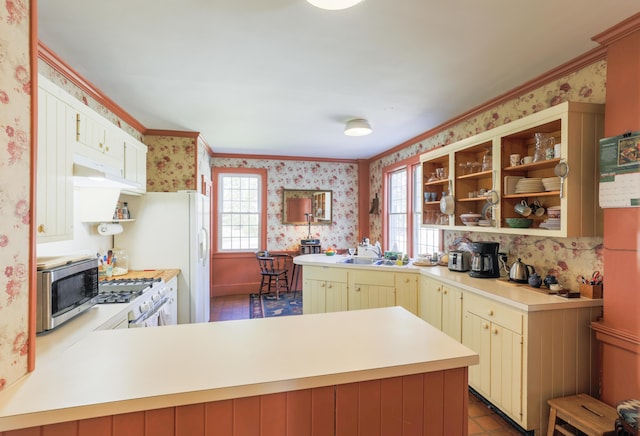 kitchen featuring wallpapered walls, a peninsula, stainless steel microwave, and a healthy amount of sunlight