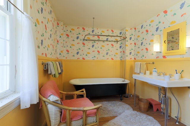 full bath featuring wallpapered walls, a soaking tub, a wainscoted wall, and wood finished floors