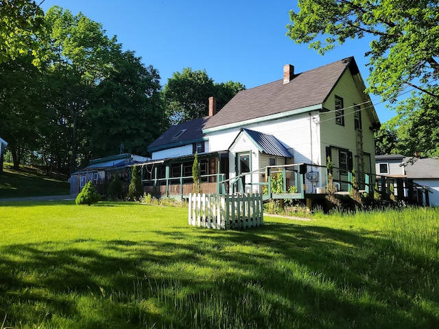 rear view of property featuring a lawn, a chimney, and a deck
