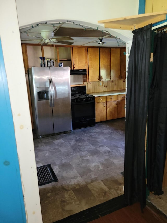 kitchen with brown cabinets, under cabinet range hood, stainless steel fridge with ice dispenser, a ceiling fan, and black gas range
