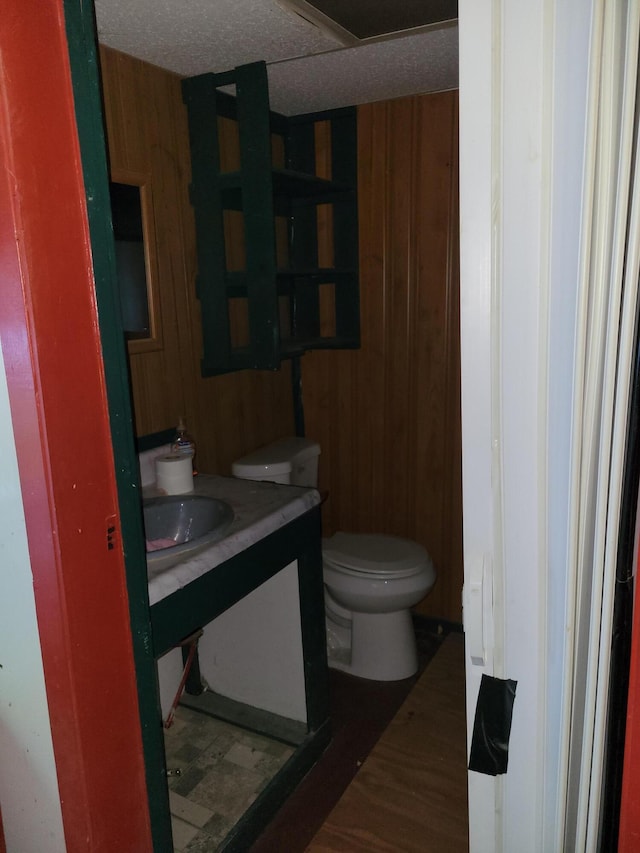 half bath featuring wood finished floors, wood walls, vanity, and toilet