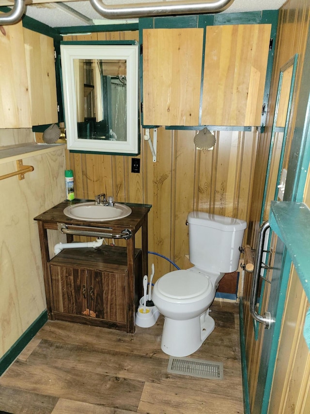 bathroom featuring wood walls, wood finished floors, visible vents, toilet, and vanity