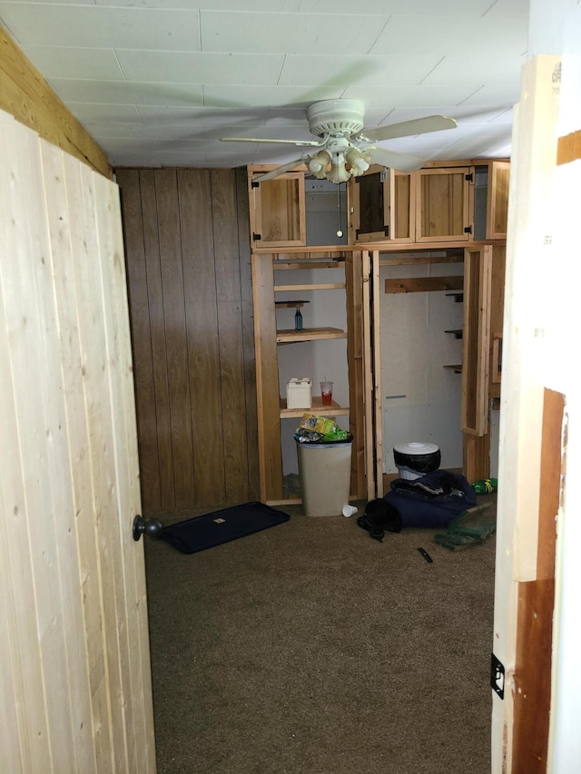 basement featuring a ceiling fan, wood walls, and carpet flooring