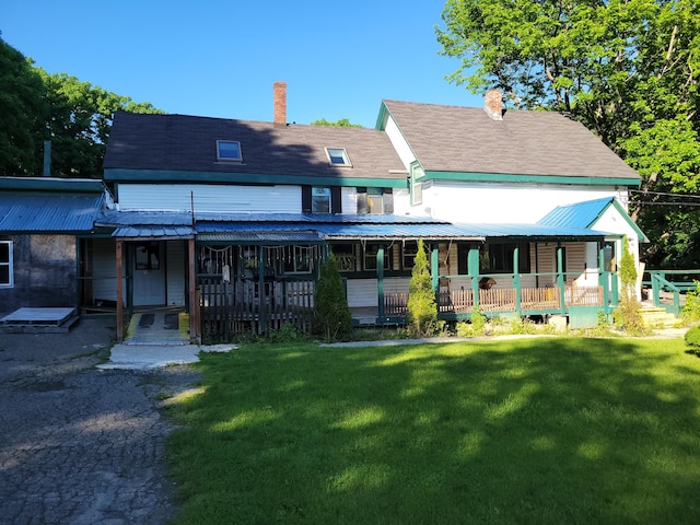 rear view of house featuring a lawn, a chimney, and covered porch