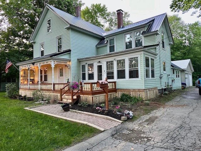 rear view of property with a chimney, aphalt driveway, a porch, and metal roof