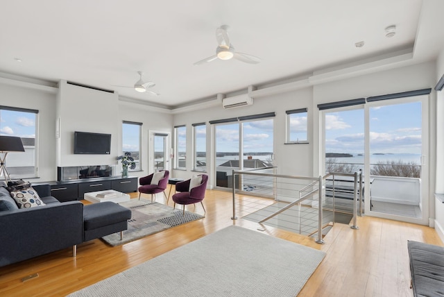 living area featuring a ceiling fan, light wood-type flooring, an AC wall unit, and a water view