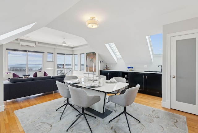 dining room with a tray ceiling, a skylight, light wood finished floors, and a wall unit AC