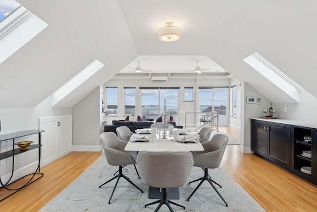 dining room with an AC wall unit, baseboards, vaulted ceiling with skylight, light wood-style flooring, and ceiling fan