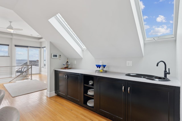 bar featuring bar area, baseboards, ceiling fan, light wood finished floors, and a sink