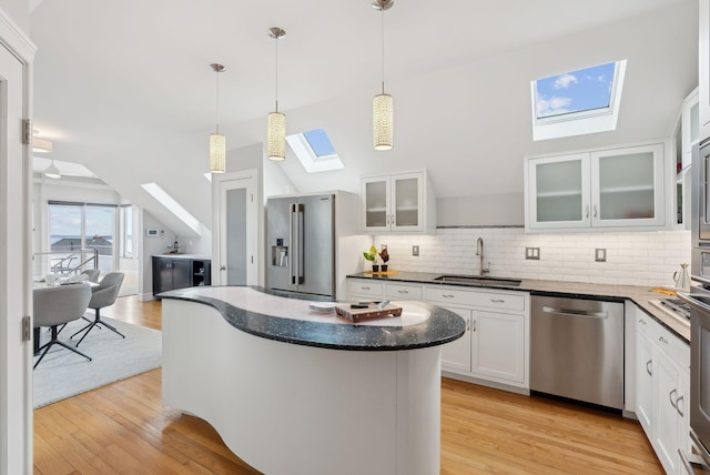kitchen with light wood-style flooring, tasteful backsplash, appliances with stainless steel finishes, a sink, and lofted ceiling with skylight