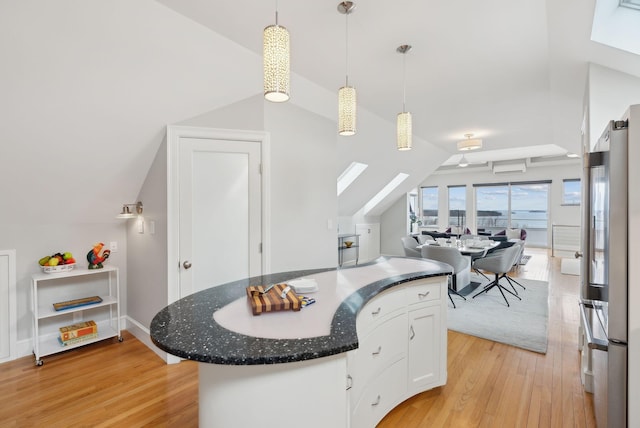 kitchen featuring open floor plan, vaulted ceiling with skylight, light wood-type flooring, and freestanding refrigerator