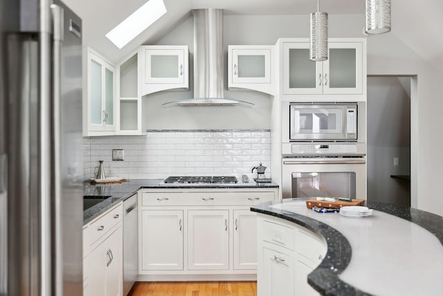 kitchen with wall chimney exhaust hood, glass insert cabinets, white cabinetry, a skylight, and stainless steel appliances