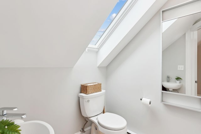 bathroom featuring toilet, a sink, baseboards, and lofted ceiling with skylight