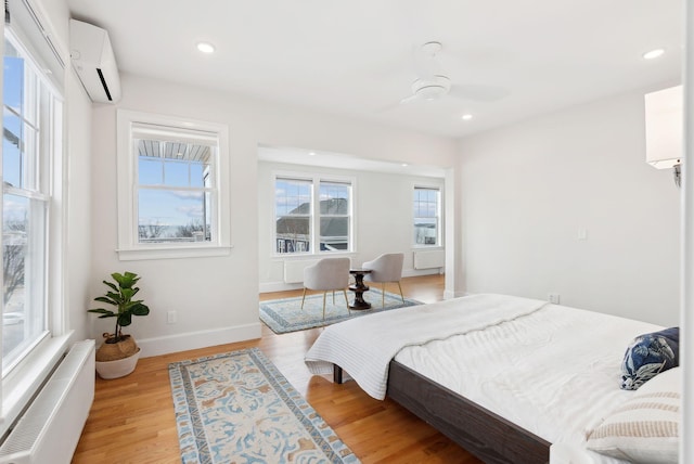 bedroom featuring light wood-type flooring, a wall unit AC, baseboards, and recessed lighting