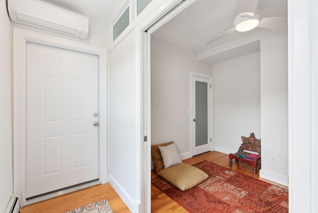 foyer with light wood-style flooring, a wall unit AC, a ceiling fan, baseboard heating, and baseboards