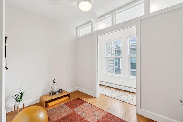 dining room featuring light wood finished floors, ceiling fan, a baseboard heating unit, and baseboards