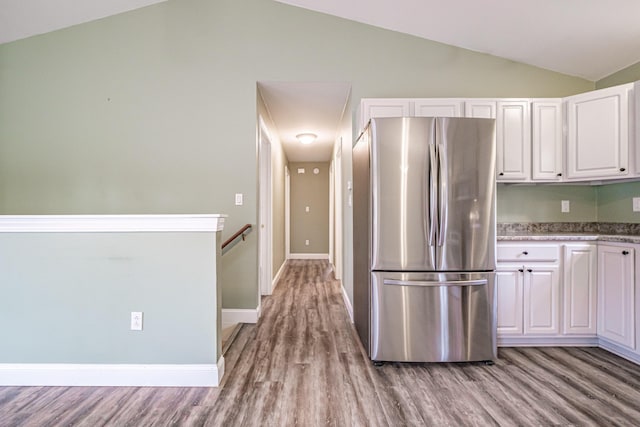 kitchen with freestanding refrigerator, vaulted ceiling, light wood-style floors, and white cabinetry