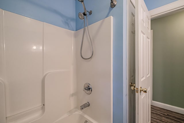 bathroom with baseboards, wood finished floors, and bathing tub / shower combination