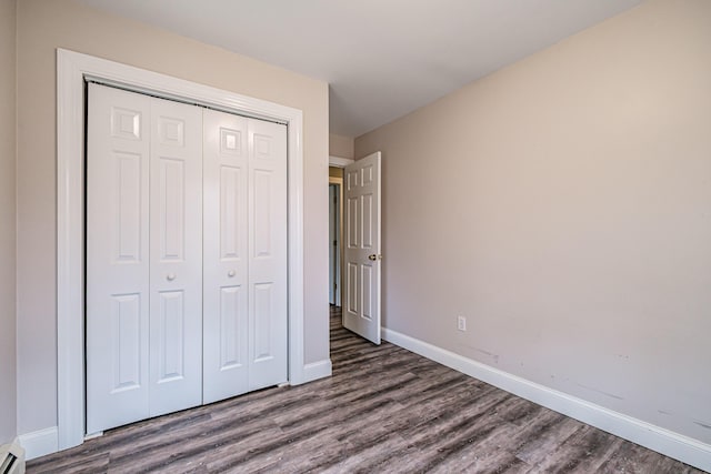 unfurnished bedroom featuring a baseboard radiator, baseboards, a closet, and dark wood-style floors
