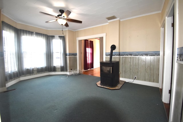131 George St, Pittsfield, ME 04967 - unfurnished living room featuring a wood stove, carpet, visible vents, a ceiling fan, and wainscoting