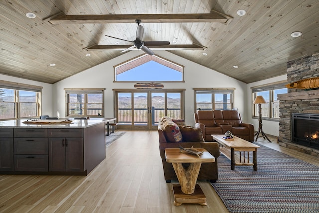 living area with wooden ceiling, a stone fireplace, a ceiling fan, light wood-style flooring, and high vaulted ceiling