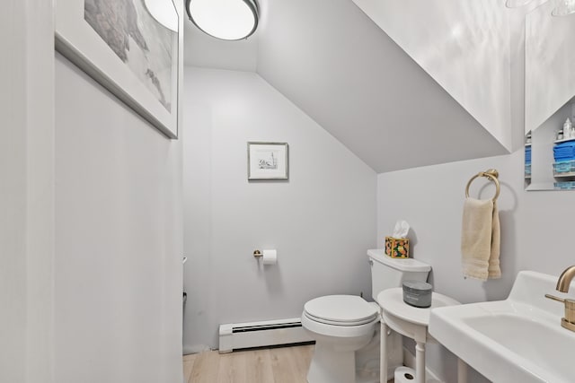 half bath with vaulted ceiling, toilet, wood finished floors, a baseboard heating unit, and a sink
