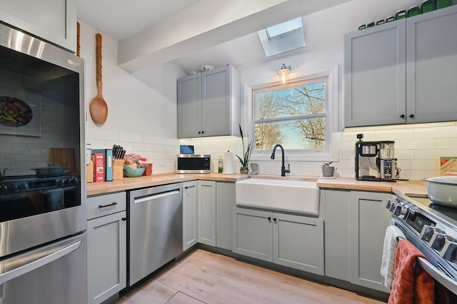 kitchen featuring appliances with stainless steel finishes, gray cabinets, wood counters, a skylight, and a sink