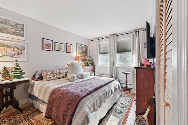 bedroom with a baseboard radiator, wood finished floors, and baseboards