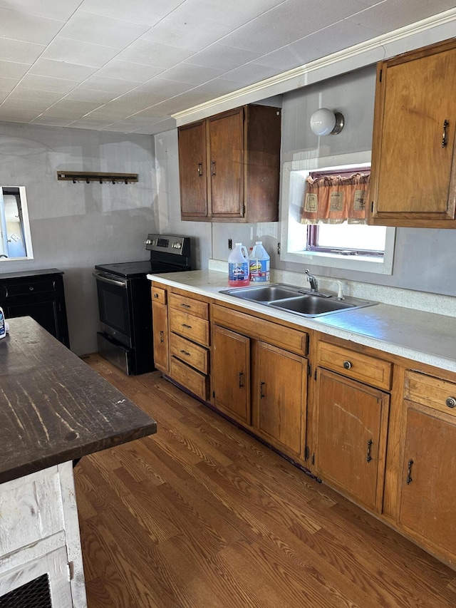 kitchen with a sink, brown cabinetry, stainless steel electric range oven, light countertops, and dark wood-style flooring