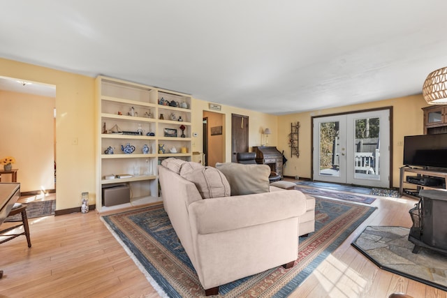 living area featuring light wood-type flooring, french doors, baseboards, and a wood stove