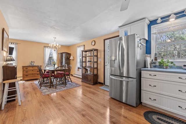 dining area featuring a baseboard heating unit, a healthy amount of sunlight, light wood-style floors, and ceiling fan with notable chandelier