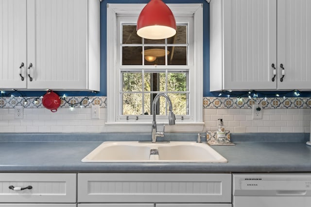 kitchen with white cabinets, dark countertops, dishwasher, a sink, and tasteful backsplash