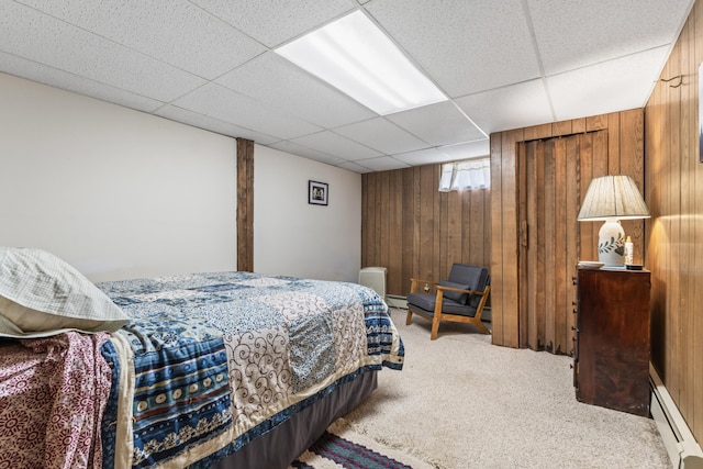 bedroom featuring a baseboard heating unit, a drop ceiling, wooden walls, and carpet