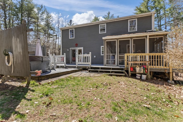rear view of house featuring a wooden deck, a sunroom, a hot tub, and a lawn