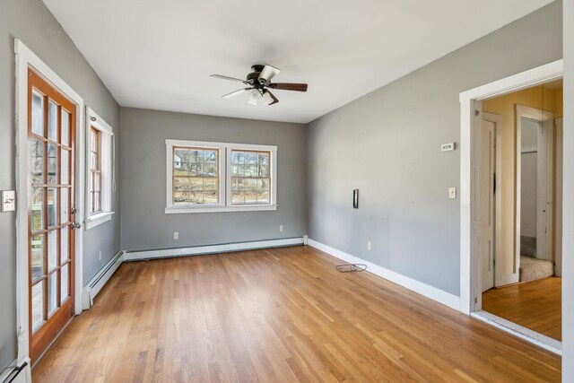 empty room with a baseboard heating unit, baseboards, a ceiling fan, and light wood-style floors