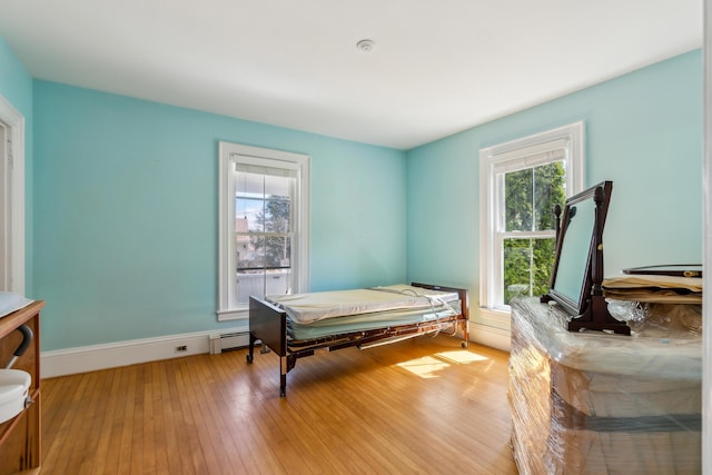bedroom with a baseboard heating unit, baseboards, and light wood-style floors
