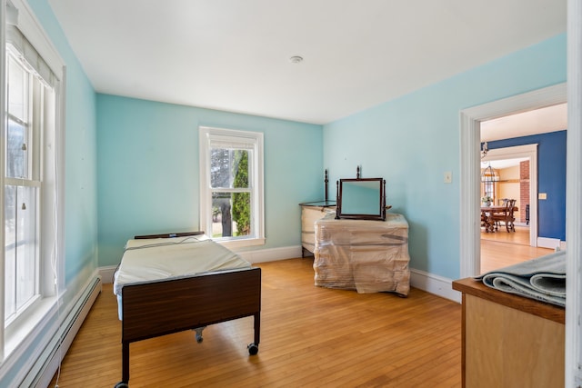 bedroom with a baseboard radiator, baseboards, and light wood-style floors