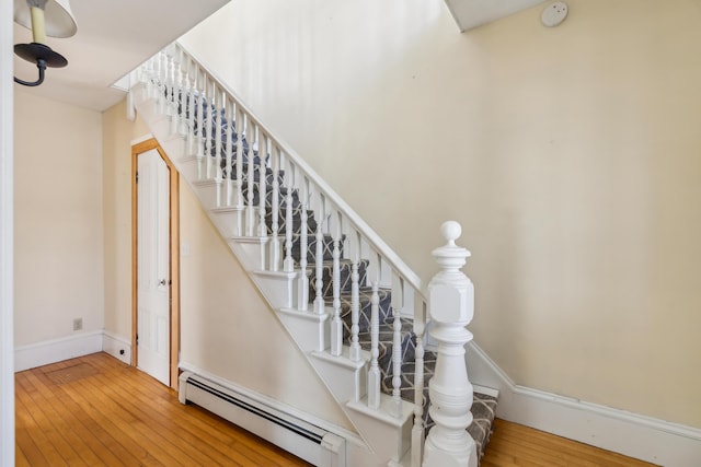 stairway with a baseboard heating unit, baseboards, and wood-type flooring