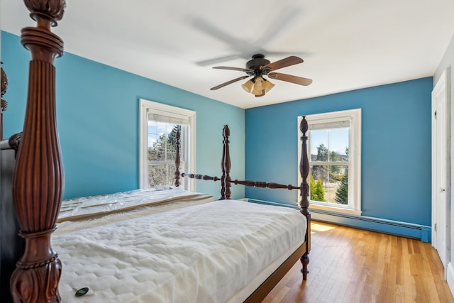 bedroom with a baseboard heating unit, hardwood / wood-style floors, ceiling fan, and multiple windows