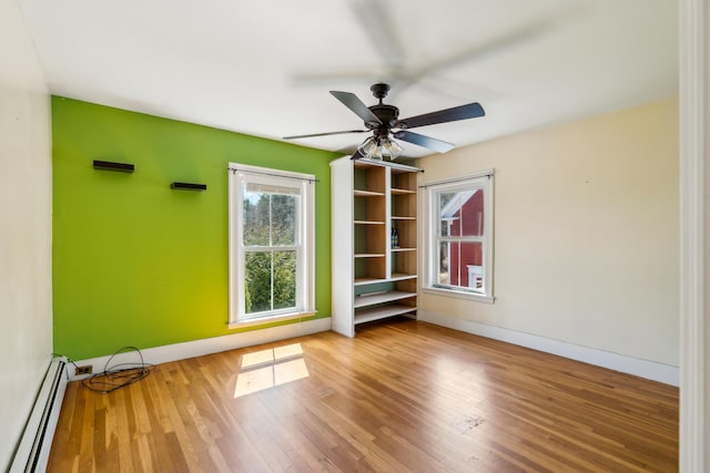 spare room with wood finished floors, a wealth of natural light, a ceiling fan, and baseboard heating