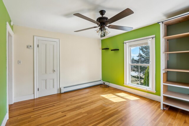 unfurnished room with baseboard heating, baseboards, a ceiling fan, and wood-type flooring