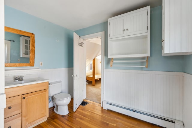 bathroom with wood finished floors, visible vents, toilet, a baseboard heating unit, and wainscoting