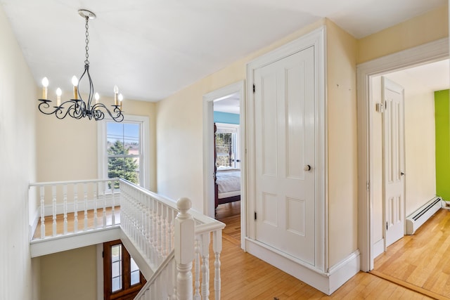 hall with baseboard heating, an upstairs landing, a chandelier, wood-type flooring, and baseboards