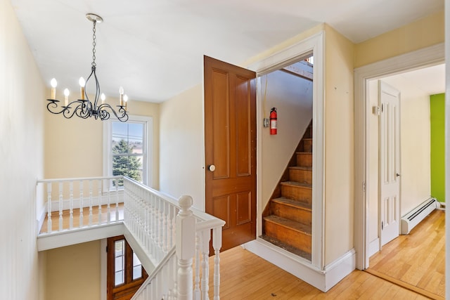 stairway with a baseboard heating unit, a chandelier, hardwood / wood-style floors, and baseboards
