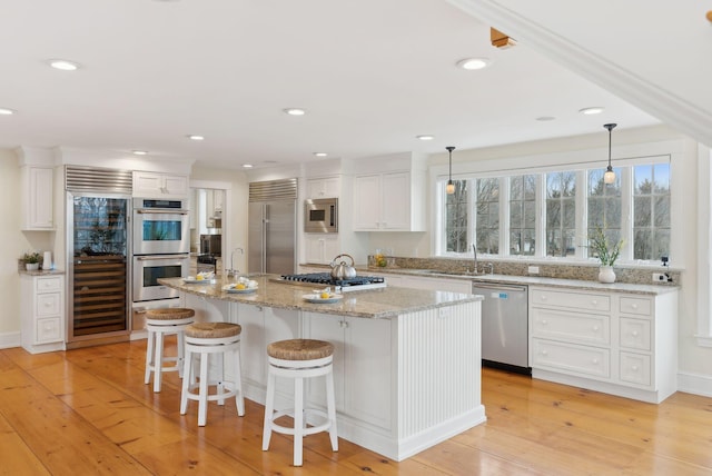 kitchen featuring a kitchen breakfast bar, a sink, a center island with sink, built in appliances, and white cabinetry