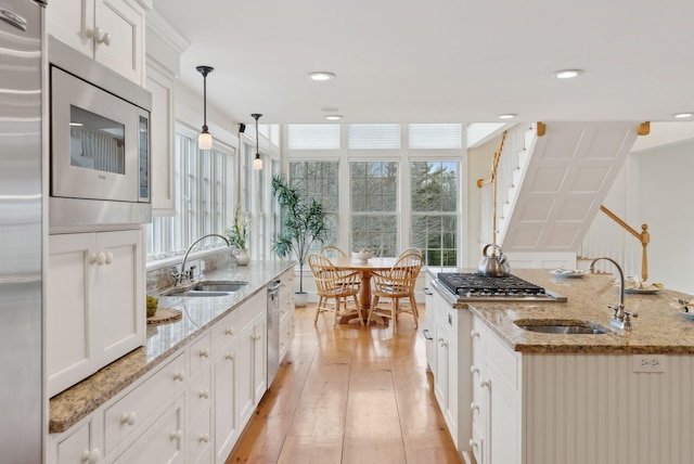 kitchen with light wood-type flooring, built in appliances, white cabinets, and a sink