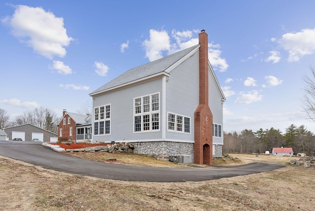 view of home's exterior with a chimney, an outdoor structure, central air condition unit, and a detached garage