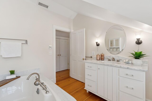 bathroom featuring lofted ceiling, wood finished floors, visible vents, vanity, and a bath