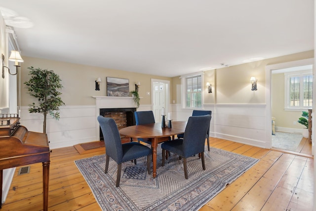 dining room featuring a fireplace, light wood-style flooring, visible vents, and wainscoting